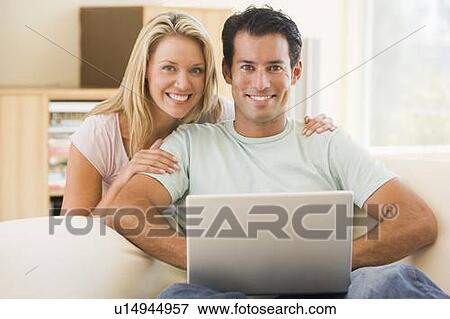 Couple in living room using laptop smiling View Large Photo Image Stock Photo - Couple in living room using laptop smiling. Fotosearch