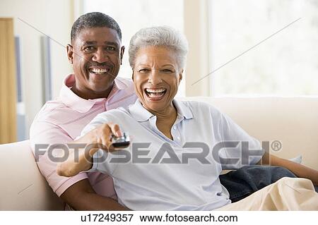 Couple in living room using remote control smiling View Large Photo Image Stock Photo - Couple in living room using remote control smiling. Fotosearch