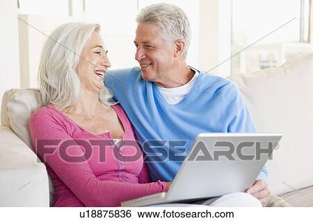 Stock Photograph - Couple in living room with laptop smiling. Fotosearch