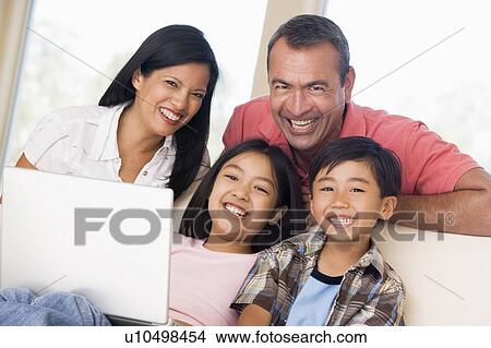 Picture - Family in living room with laptop smiling. Fotosearch