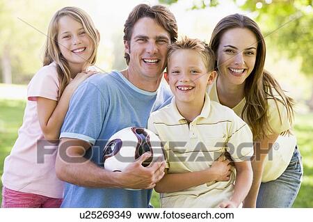 Stock Photo - Family standing outdoors holding volleyball smiling. Fotosearch