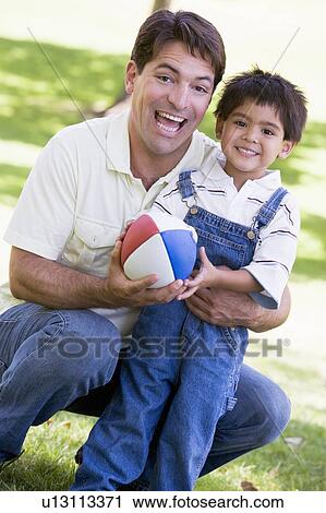 Stock Image - Man and young boy outdoors with football smiling. Fotosearch