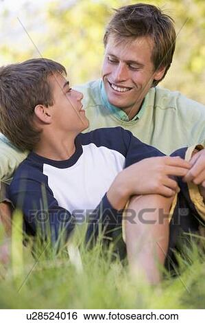 Stock Photograph - Man and young boy sitting outdoors smiling. Fotosearch