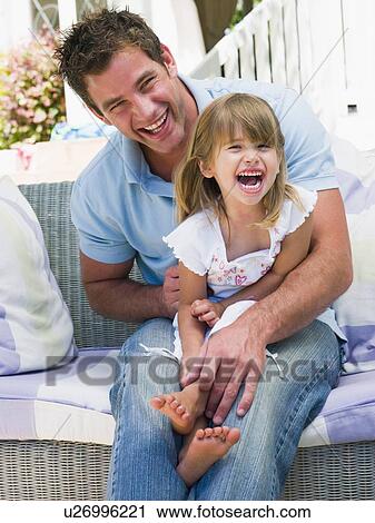 Stock Image - Man and young girl sitting on patio laughing. Fotosearch