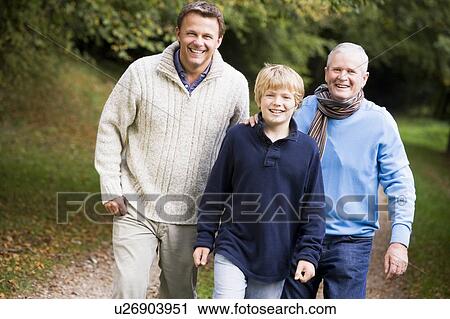 Stock Image - Two men and young boy walking on path outdoors smiling (selective focus). Fotosearch