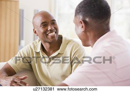 Two men in living room talking and smiling View Large Photo Image Stock Image - Two men in living room talking and smiling. Fotosearch