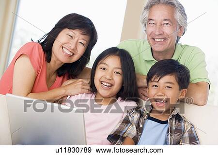 Stock Photo - Couple with two young children in living room with laptop smiling. Fotosearch