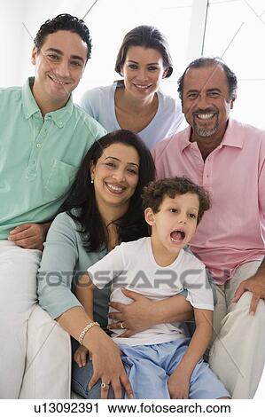 Stock Image - Family sitting in living room smiling (high key). Fotosearch