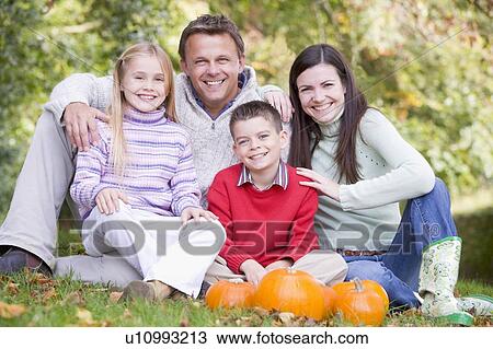 Stock Image - Family sitting on grass with pumpkins smiling. Fotosearch