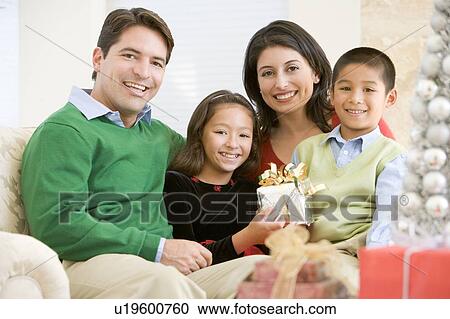 Stock Image - Family Sitting On Sofa Together, Holding A Christmas Gift. Fotosearch