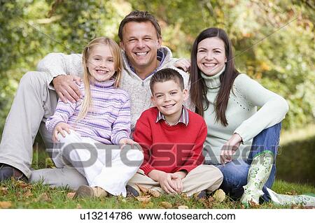 Family sitting outdoors smiling (selective focus) View Large Photo Image Stock Photograph - Family sitting outdoors smiling (selective focus). Fotosearch