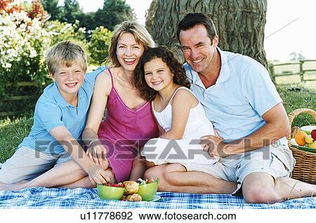 Stock Image - Family sitting outdoors with picnic smiling. Fotosearch