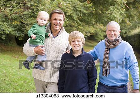 Stock Image - Two men and two young children standing on path outdoors smiling (selective focus). Fotosearch