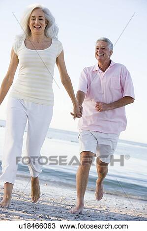 Stock Image - Couple at the beach holding hands and smiling. Fotosearch