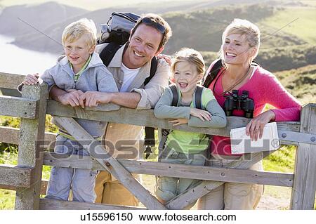 Stock Image - Family on cliffside path leaning on fence and smiling. Fotosearch