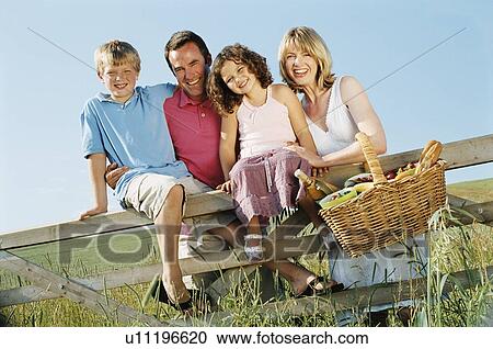 Stock Image - Family outdoors by fence with picnic basket smiling. Fotosearch
