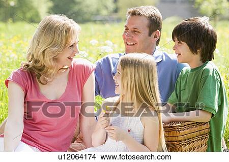 Picture - Family sitting outdoors with picnic basket smiling. Fotosearch