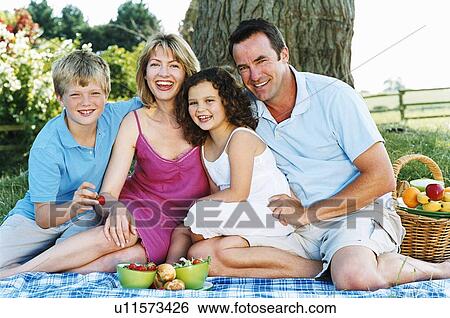 Stock Photograph - Family sitting outdoors with picnic smiling. Fotosearch