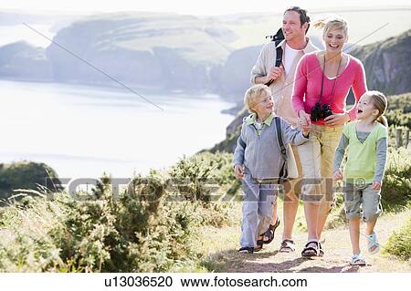 Stock Image - Family walking on cliffside path holding hands and smiling. Fotosearch