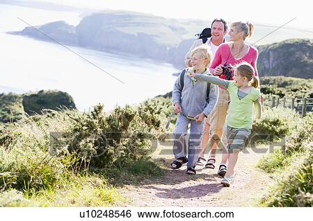 Stock Photograph - Family walking on cliffside path pointing and smiling. Fotosearch