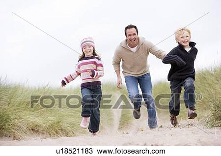Stock Image - Father and two young children running at beach smiling. Fotosearch
