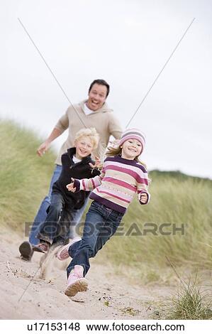 Stock Photo - Father and two young children running at beach smiling. Fotosearch