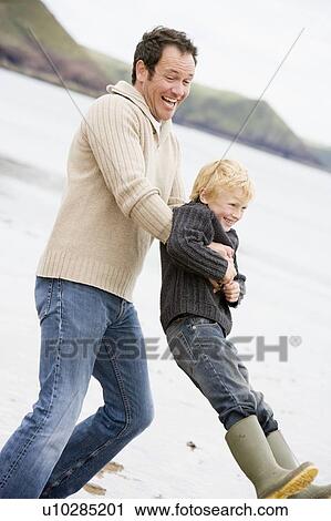 Stock Image - Father holding son at beach smiling. Fotosearch