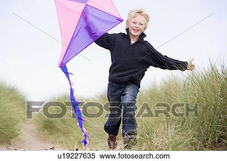 Stock Photography - Young boy running on beach with kite smiling. Fotosearch