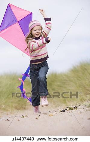 Stock Photo - Young girl on beach with kite smiling. Fotosearch