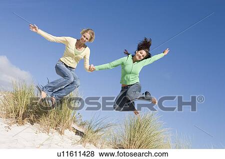 Stock Photo - Young woman jumping on a sand hill. Fotosearch