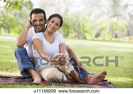 Couple sitting outdoors in park smiling (selective focus) View Large Photo Image Stock Photo - Couple sitting outdoors in park smiling (selective focus). Fotosearch