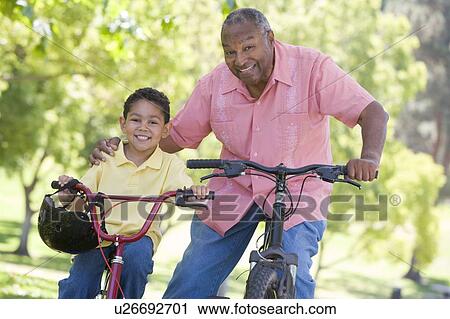 Stock Image - Grandfather and grandson on bikes outdoors smiling. Fotosearch