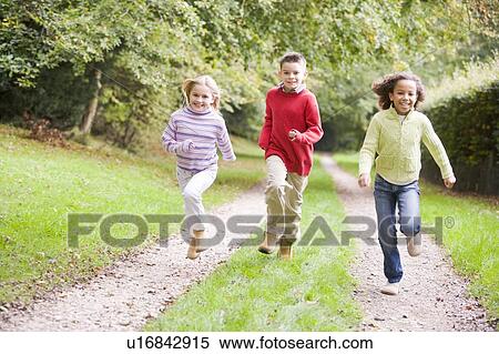 Stock Photography - Three young friends running on a path outdoors smiling. Fotosearch