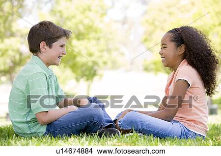 Picture - Tow young friends sitting outdoors looking at each other and smiling. Fotosearch
