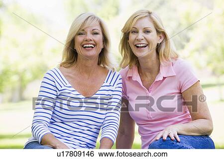 Two women sitting outdoors smiling View Large Photo Image Stock Photograph - Two women sitting outdoors smiling. Fotosearch