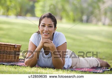 Stock Photography - Woman lying outdoors at park with picnic basket smiling (selective focus). Fotosearch