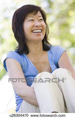 Stock Image - Woman sitting outdoors smiling. Fotosearch