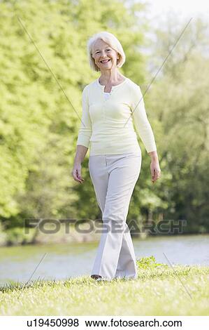Woman walking outdoors at park by lake smiling View Large Photo Image Stock Photo - Woman walking outdoors at park by lake smiling. Fotosearch