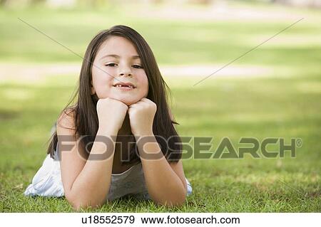 Stock Photo - Young girl outdoors lying in grass and smiling (selective focus). Fotosearch
