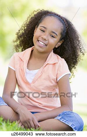 Stock Image - Young girl sitting outdoors smiling. Fotosearch