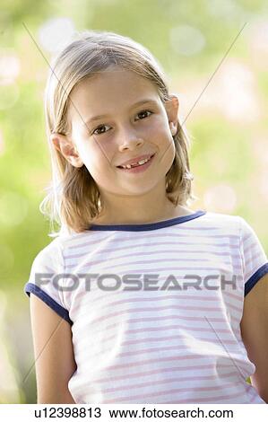 Stock Image - Young girl standing outdoors smiling. Fotosearch