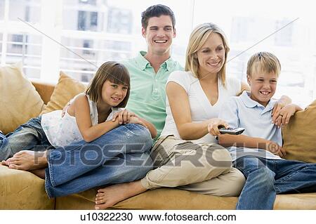 Stock Image - Family sitting in living room with remote control smiling. Fotosearch
