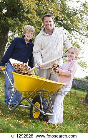 Father and children outdoors shoveling leaves into wheelbarrow and smiling (selective focus) View Large Photo Image Stock Photo - Father and children outdoors shoveling leaves into wheelbarrow and smiling (selective focus). Fotosearch