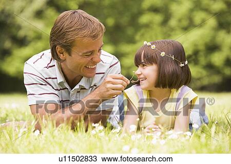 Stock Image - Father and daughter lying outdoors with flowers smiling. Fotosearch