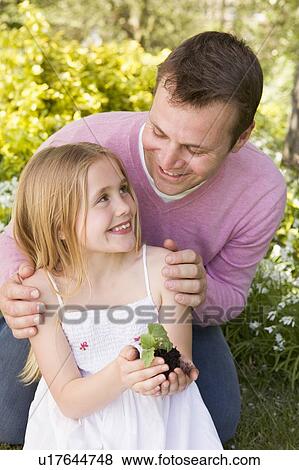 Stock Photo - Father and daughter outdoors holding plant smiling. Fotosearch