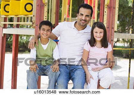 Father and two children sitting on playground structure smiling (selective focus) View Large Photo Image Stock Photo - Father and two children sitting on playground structure smiling (selective focus). Fotosearch