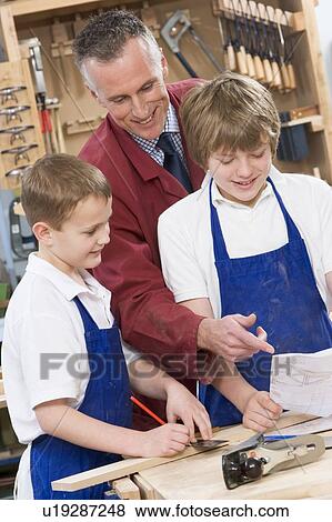 Stock Photo - Male students reviewing woodworking plans with teacher. Fotosearch