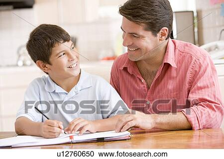 Stock Image - Man helping young boy in kitchen doing homework and smiling. Fotosearch