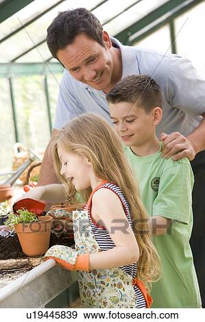 Man in greenhouse helping two young children putting soil in pot View Large Photo Image Stock Photo - Man in greenhouse helping two young children putting soil in pot. Fotosearch