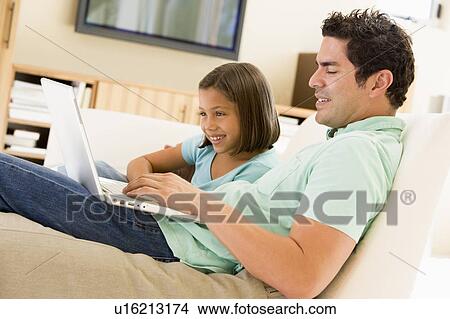 Picture - Man with young girl in living room with laptop smiling. Fotosearch